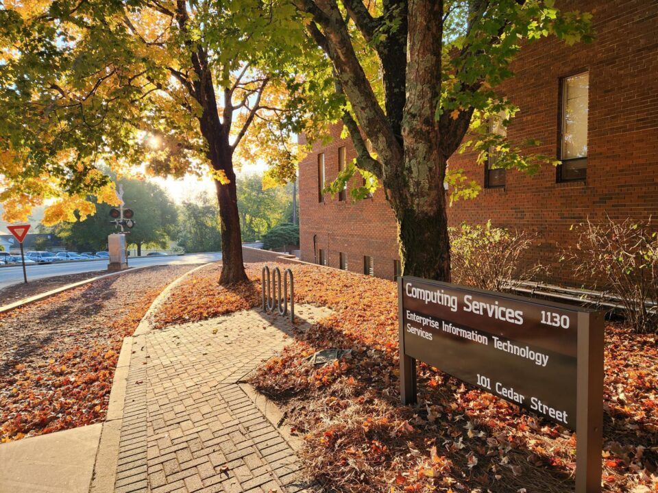 A picture of the entrance to the Computing Service building with autumn foilage and a setting sun.